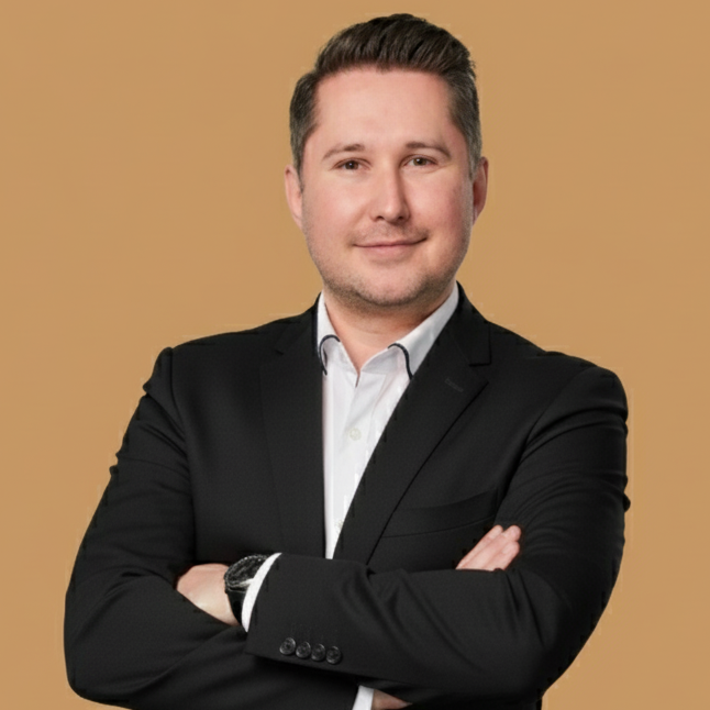 Pascal Grunenberg Mann in Anzug mit verschränkten Armen, lächelt freundlich in die Kamera.